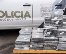 Tabletes de droga empilhados ao lado de uma viatura
