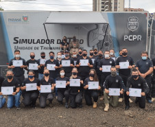 Participantes do curso reunidos para foto ao lado de simulador de tiro