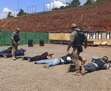 Policiais civis deitados, apontando as armas para alvos de papel, observados pelos instrutores