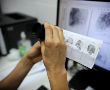 Foto mostra papiloscopista analisando digitais com lupa