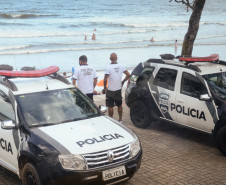 Dois policiais civis entre duas viaturas, observam o movimento dos veranistas