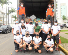 Policiais civis e servidores da Defesa Civil posando para foto junto a caminhao com produtos arrecadados