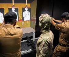 Dois policiais militares apontando as armas para tela de simulador da polícia civil