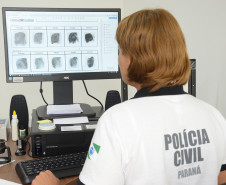 Policial civil analisando digitais em tela de monitor