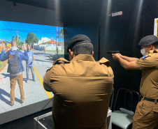Dois policiais militares apontando as armas para tela de simulador da polícia civil