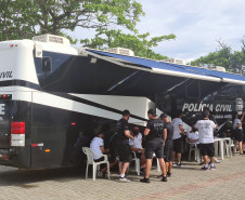 Diversos policiais civis reunidos ao lado do ônibus com a delegacia móvel