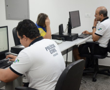 Dois policiais civis. Um deles atendendo veranista na delegacia