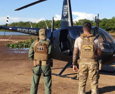 Policiais de costas, ao lado de helicóptero da polícia civil