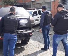 Três policiais civis ao lado de viatura