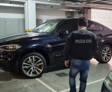 Policial civil de costas observando veículo de luxo estacionado