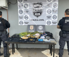 Dois policiais de costas ao lado de mesa com produtos apreendidos