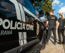 Dois policiais civis ao lado de viatura