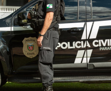 Policial civil ao ao lado de viatura