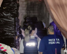 Policial civil e servidora da Receita Federal observam depósito com cigarros contrabandeados