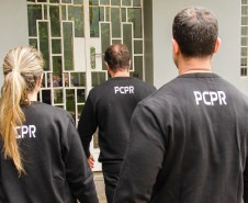 Três policiais civis de costas entrando em delegacia