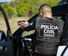 Policial civil ao lado de viatura apontando arma