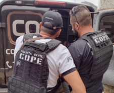 Dois policiais civis ao lado de viatura