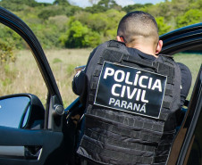 Policial civil apontando arma ao lado de viatura