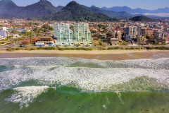 Litoral paranaense, com mar em primeiro plano e, ao fundo, prédios e montanhas.