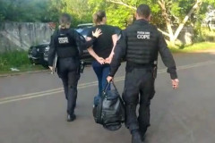 Dois policiais civis encaminhando um dos presos até a viatura