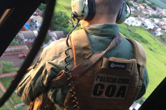 Policial civil dando apoio a bordo de helicóptero para equipes que atuam no solo