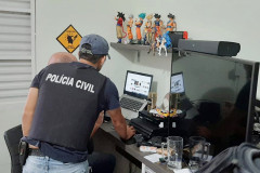Policiais civis analisam notebook no interior de um quarto
