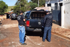 Policiais civis em pé, ao lado de uma viatura estacionada