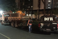 Policial civil ao lado de viatura, averiguando material na carroceria de um caminhão