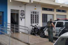Policial civil ao lado de viatura, em frente à delegacia