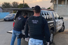Dois policiais civis atrás de uma viatura com a tampa do porta-malas aberta