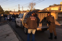 Dois policiais fechando porta-malas de viatura. Em frente, vários policiais reunidos.