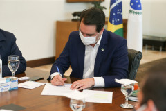 Governador sentado à mesa, assinando documento