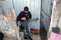 Policial saindo por portão de residência com skate e faca nas mãos