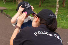 Policial civil agachada, colocando boné em criança