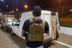 Policial civil em primeiro plano, de costas. Em segundo plano, veículos apreendidos