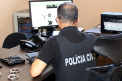 Policial ao computador. Na mesa, arma e algemas