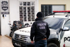 Policial civil ao lado de viatura, em frente à delegacia