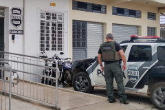 Policial civil ao lado de viatura, em frente a delegacia