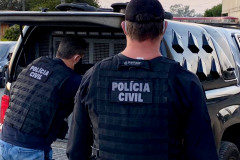 Dois policiais civis atras de uma viatura com o porta-malas aberto