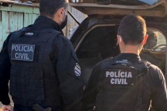 Dois policiais civis de costas, ao lado de viatura