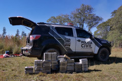 Diversos tabletes de droga empilhados ao lado de viatura da polícia civil