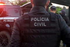 Policial civil de costas, próximo à viatura