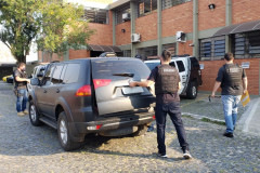 Trêspoliciais civis, um deles abrindo a tampa do porta-malas da viatura