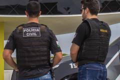 Dois policiais de costas, ao lado de viatura