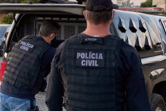 Dois policiais civis ao lado de viatura