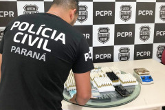 Policial civil de costas, organizando sobre uma mesa o material apreendido