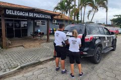 Policiais civis fechando tampa do porta-malas de viatura, em frente à delegacia 