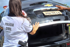 Policiais civis fechando tampa de porta-malas de viatura