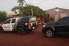 Policiais civis investigando local. Em frente à casa, uma viatura