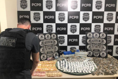 Policial civil de costas, organizando material apreendido sobre uma mesa. Ao fundo, banner com logo da PCPR.